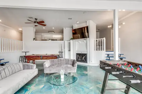 Game room with pool table, foosball table, and wall-mounted TV above a white brick fireplace, with the kitchen visible beyond at Brompton Manor, Oklahoma City