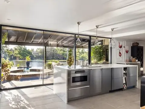 Modern kitchen with marble waterfall island, geometric pendant lights, and floor-to-ceiling glass walls facing the hot tub and lake at Lakefront Manor, Oklahoma City