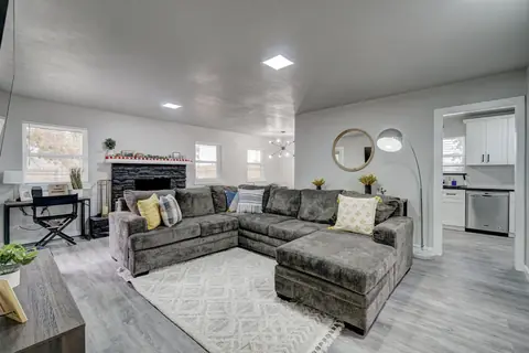 Living room with a large gray sectional, black stone fireplace, round wood-framed mirror, and arc floor lamp opening to the kitchen at The Village Manor, Oklahoma City